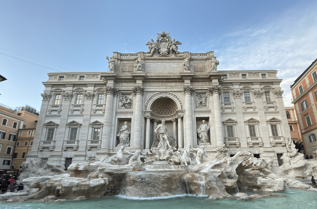 The ornate Baroque sculptures and turquoise water of the Trevi Fountain in Rome, a historic landmark for those looking to escape US cities for a European vacation.