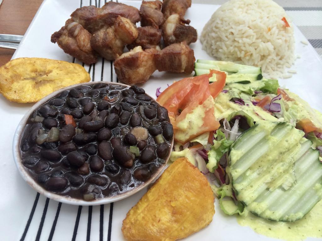 A traditional Casado plate featuring black beans, white rice, fried plantains, grilled pork, and a fresh salad, a staple dish for those who travel Costa Rica.
