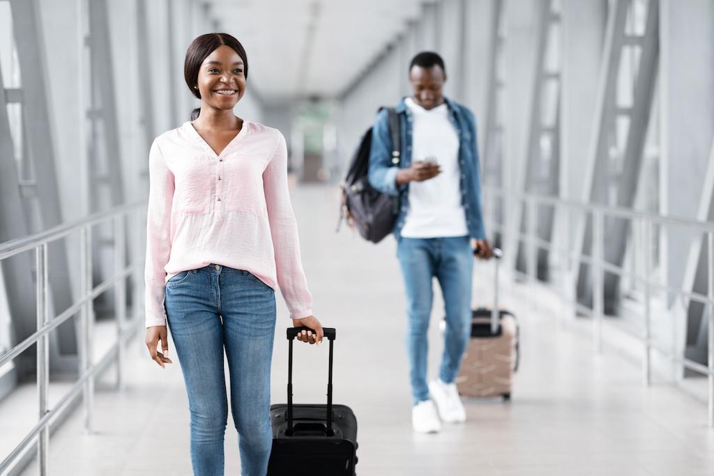 Two travelers smiling while walking through an airport with their luggage, highlighting the importance of a flexible trip cancellation policy.