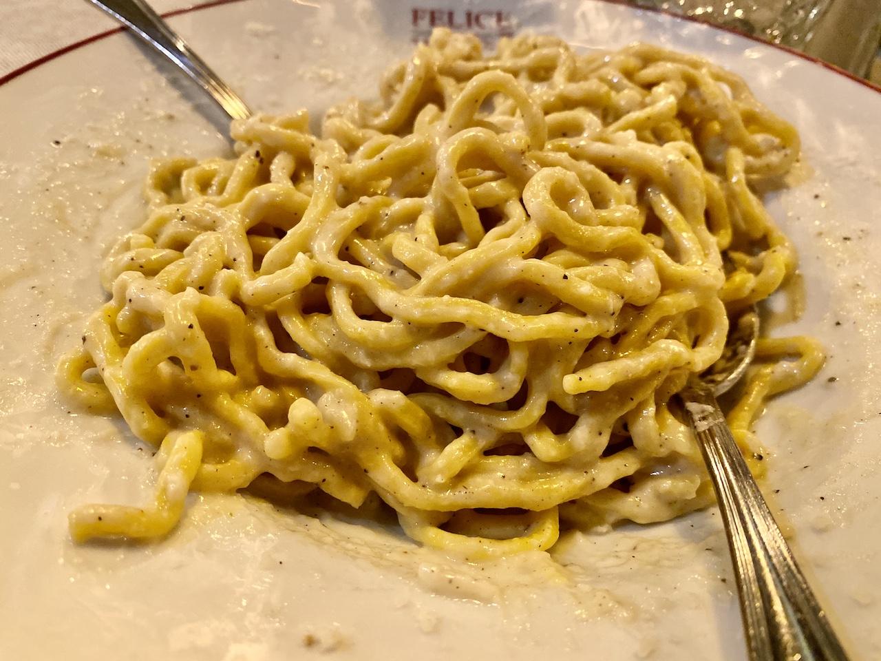A close-up view of a large serving of fresh cacio e pepe pasta with a thick, creamy cheese and black pepper sauce on a white plate, a dish for those applying experience to finding authentic Roman cuisine.