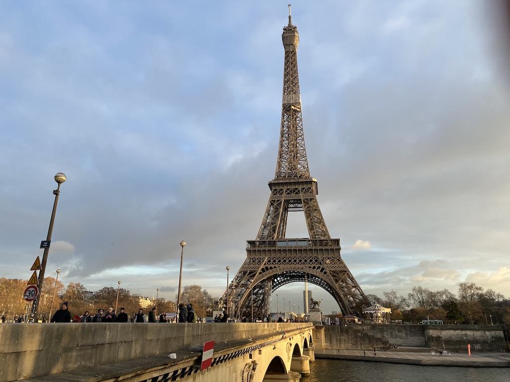 The Eiffel Tower stands tall over the Seine River and the Pont d'Iéna bridge in Paris during a cloudy afternoon, a classic landmark for family travel.