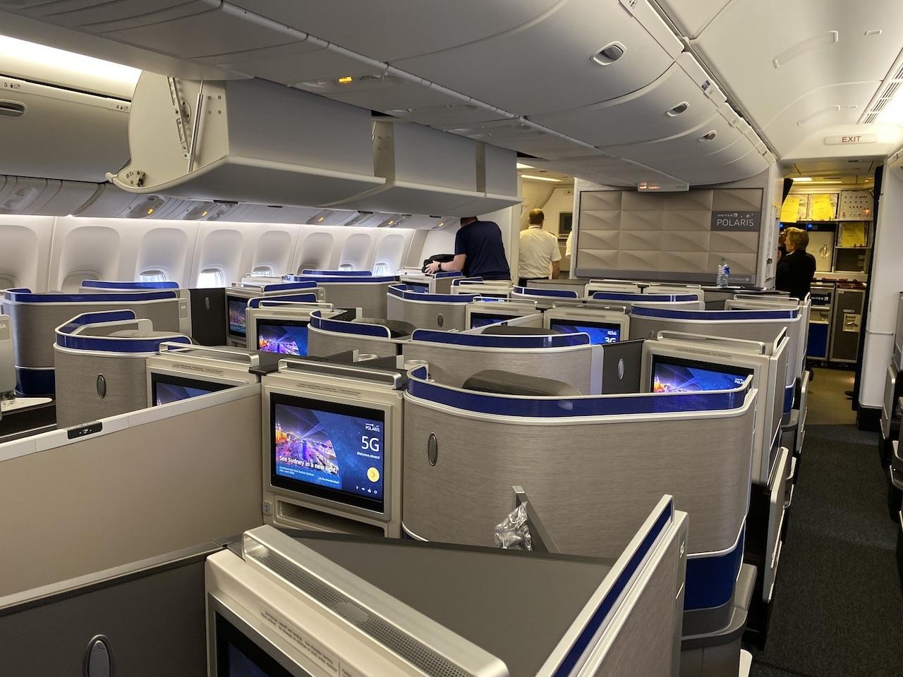 The business class cabin of a commercial aircraft with individual pods and entertainment screens, showcasing a luxury travel experience often booked by redeeming frequent flyer miles.