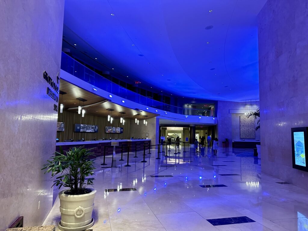 A sleek hotel lobby at the Hyatt Regency Orlando with blue neon ceiling lights leading to the Grotto Pool, a perk of hotel loyalty programs.