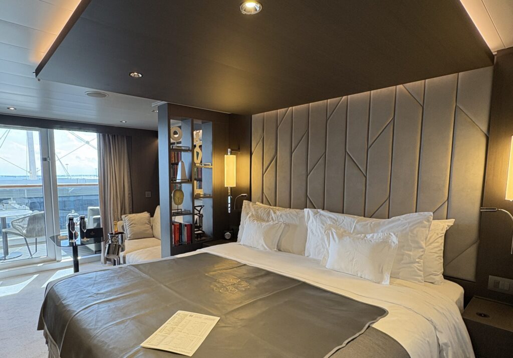 Interior of a luxury hotel or cruise suite with a modern king bed and private balcony, highlighting high-end accommodation and travel comfort.