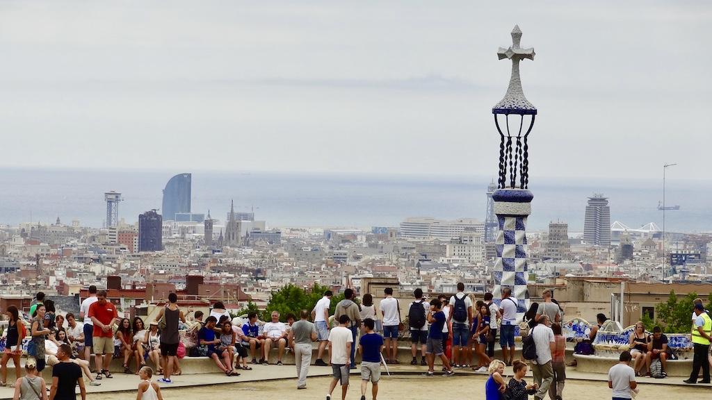Tourists gather at a scenic overlook in Park Güell to admire the iconic mosaic towers and cityscape during a trip to Barcelona.
