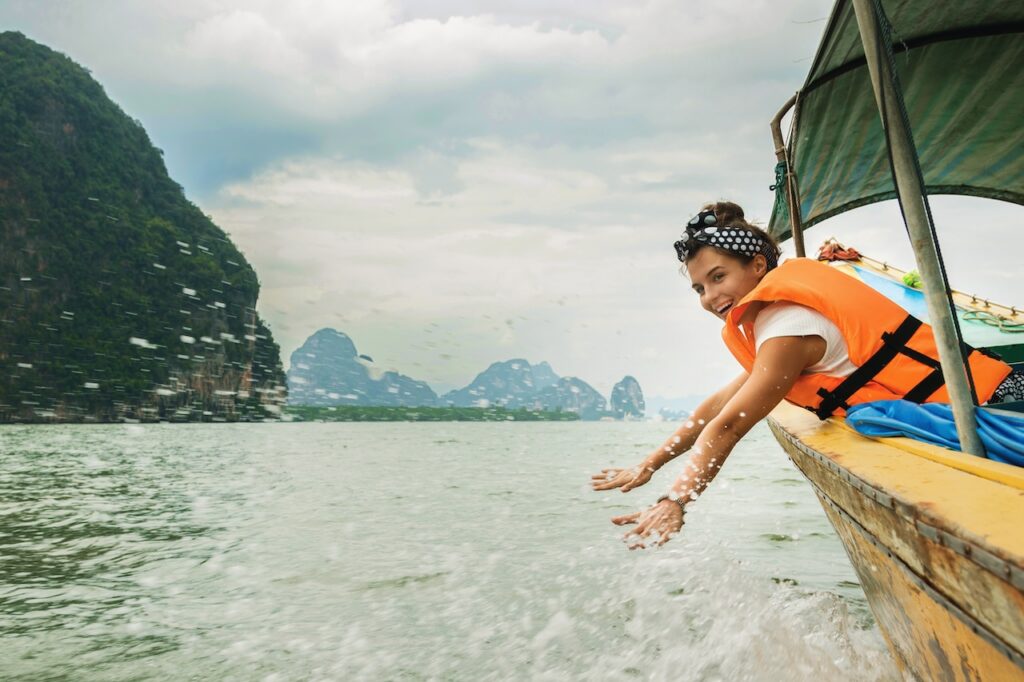 Traveler enjoying a sunny beach day with longtail boats and limestone cliffs, highlighting the ideal weather for island hopping during Thailand's peak season.
