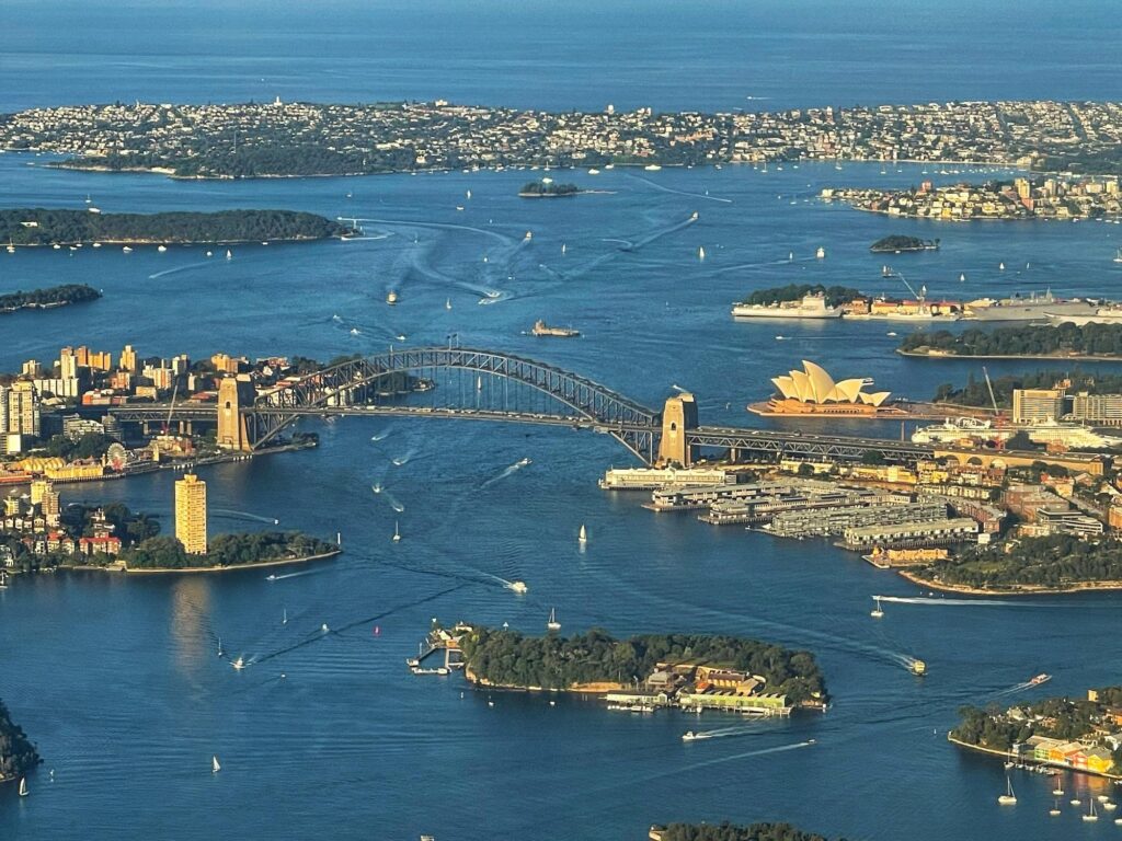 An aerial view of the iconic Sydney Opera House and the Sydney Harbour Bridge spanning the water, highlighting two of the most famous attractions in Sydney.