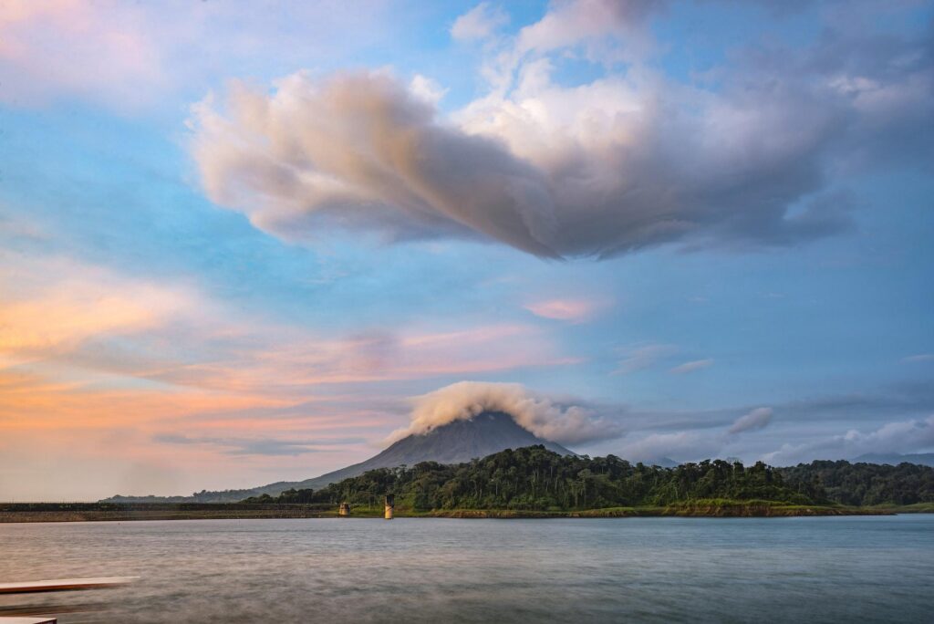 A serene view of a volcano shrouded in clouds overlooking a calm lake at sunset, located near a luxury resort in Costa Rica.