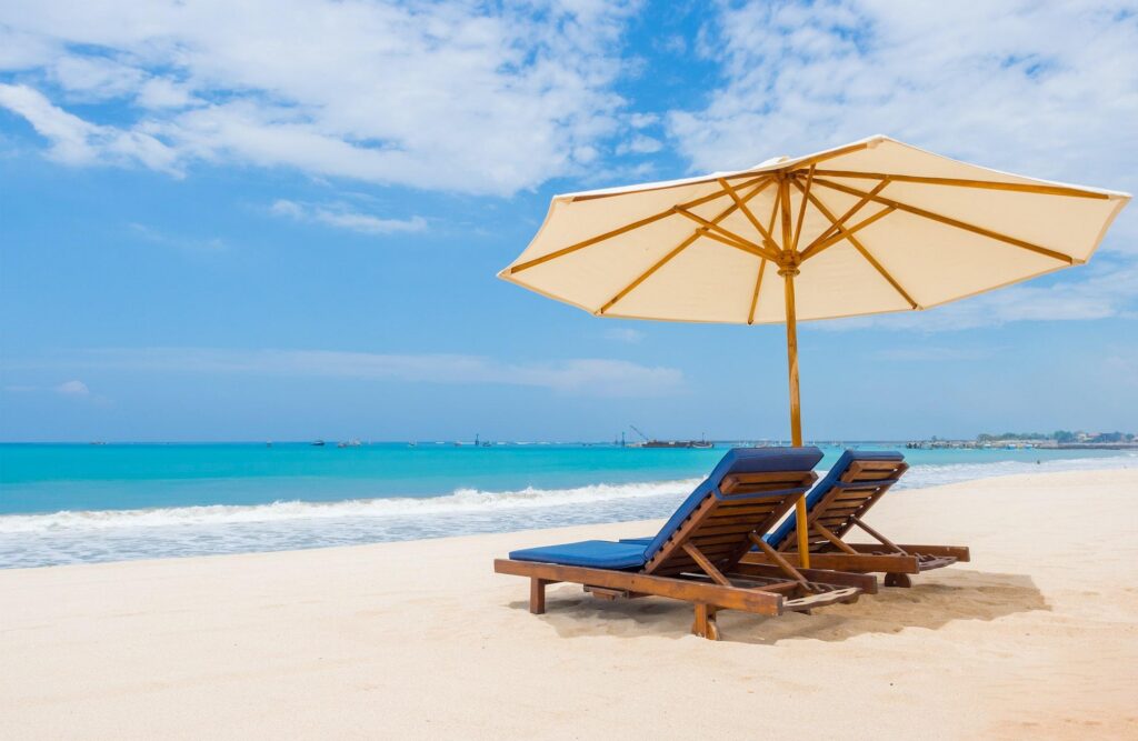 A tropical beach with lounge chairs under a white umbrella, overlooking turquoise waters, capturing the luxury cruise experience.