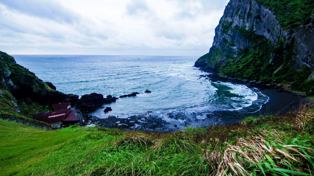 A scenic view of the lush volcanic coastline near Jeju City, featuring the iconic Seongsan Ilchulbong tuff cone and the deep blue sea.