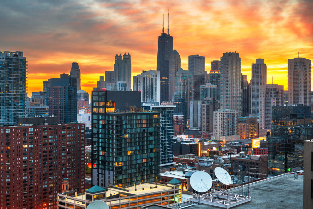 A scenic dusk view of the Chicago skyline featuring iconic skyscrapers like the Willis Tower, as seen from a high vantage point. The glowing city lights and dramatic sunset sky highlight the prime locations of the best boutique hotels Chicago has to offer for travelers seeking luxury and style.