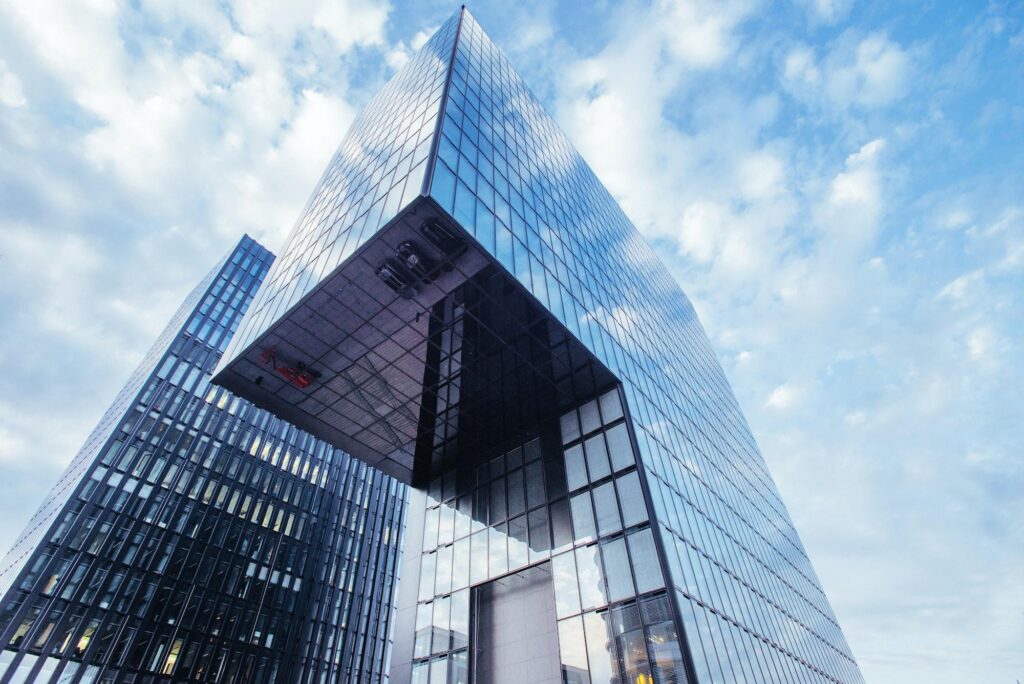 Low-angle shot of a modern glass skyscraper with cantilevered section reflecting blue sky, typical of contemporary Hyatt Hotels architecture.