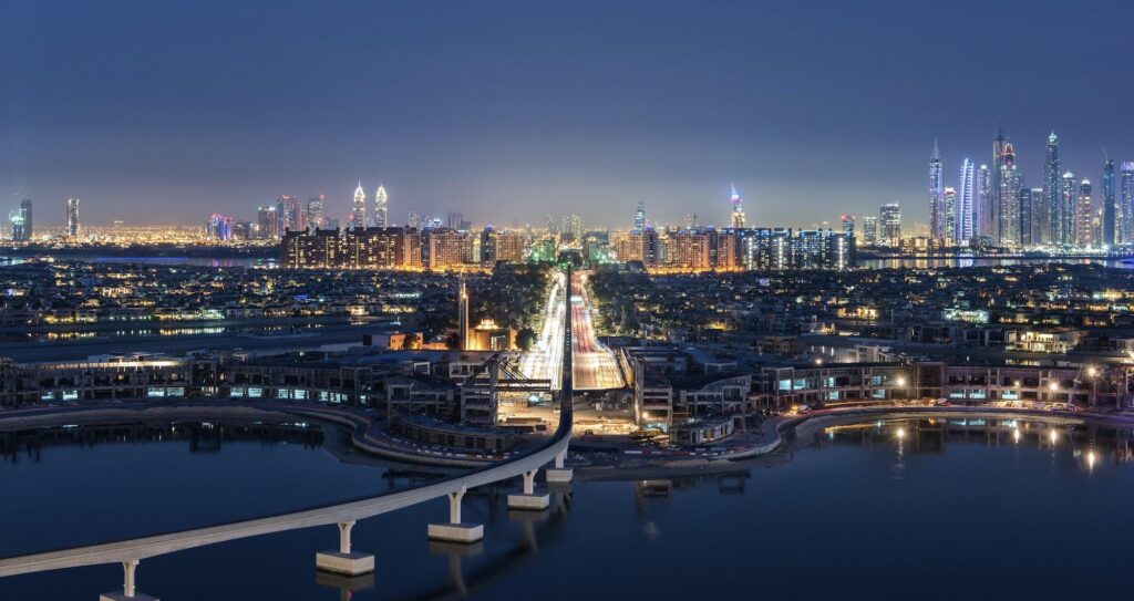 Aerial night view of illuminated Dubai landmarks, including the Burj Khalifa and the glowing highways of the Downtown skyline.