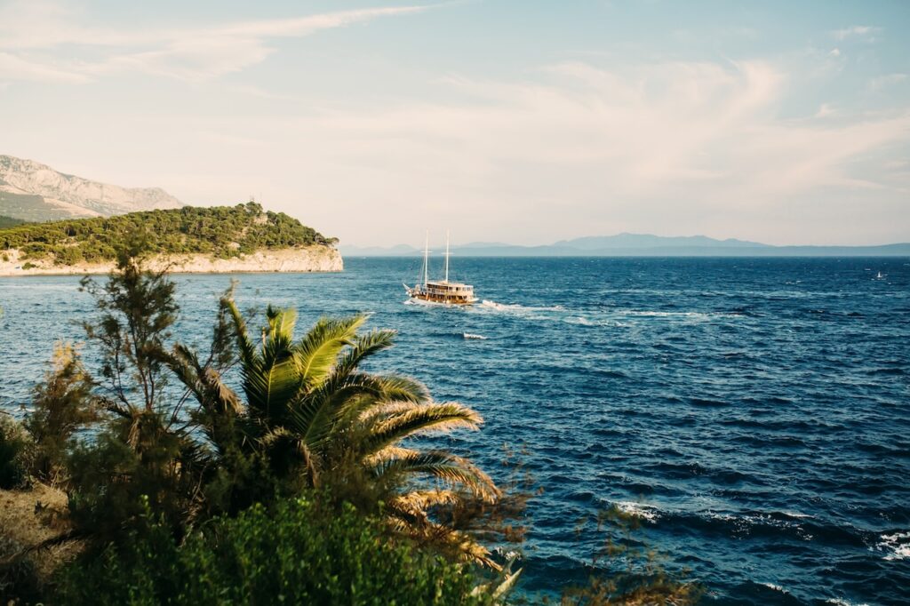 Sailboat on the deep blue Adriatic Sea near a lush, rocky coastline, representing the scenic exploration of a Silversea Croatia cruise.