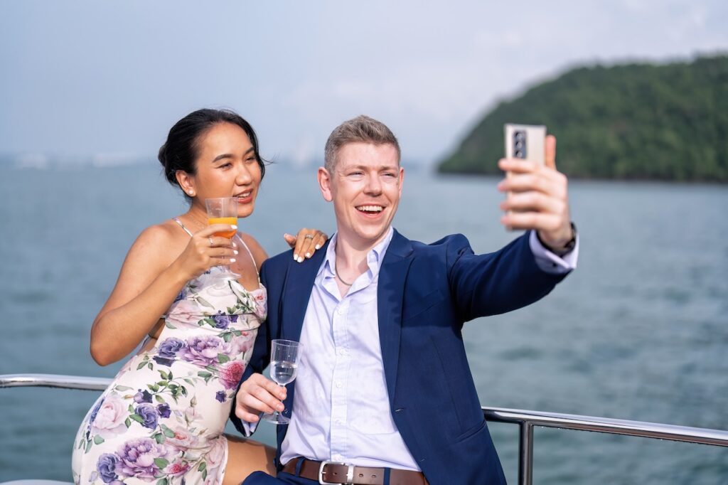 Smiling couple taking a selfie while on a boat trip, highlighting a happy luxury ocean travel experience with a scenic sea view background.