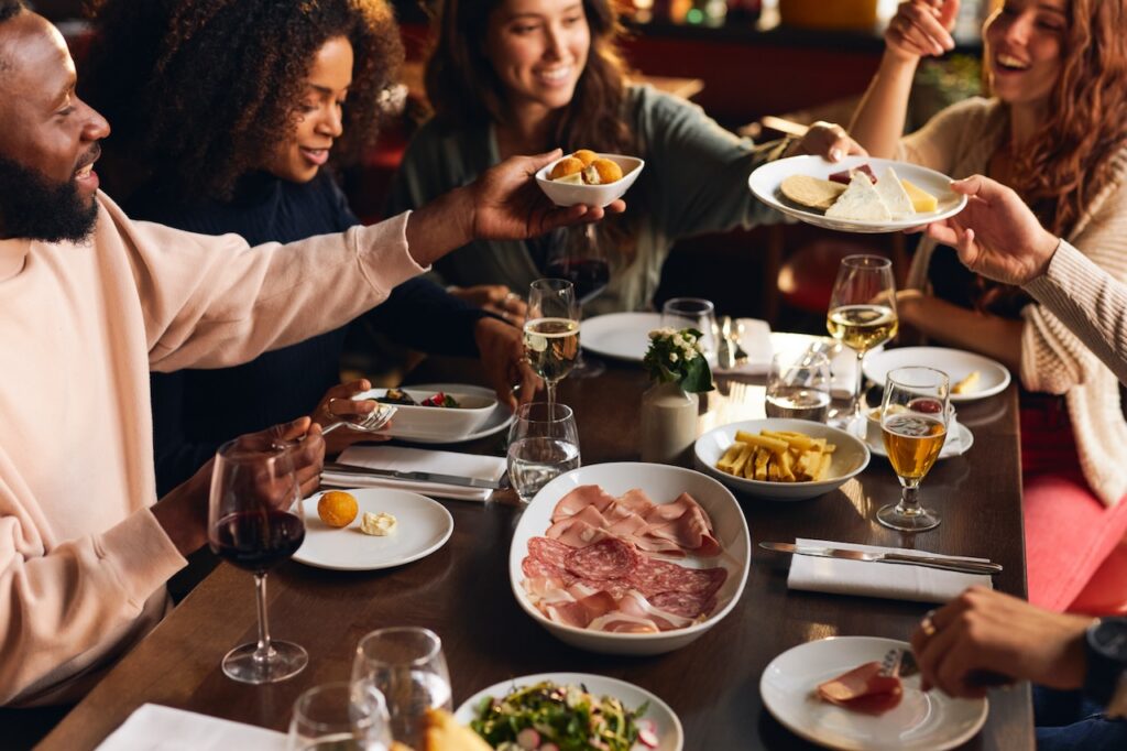 Four friends share charcuterie, cheeses, and drinks at a cozy, dimly lit table, enjoying a warm and convivial evening.”