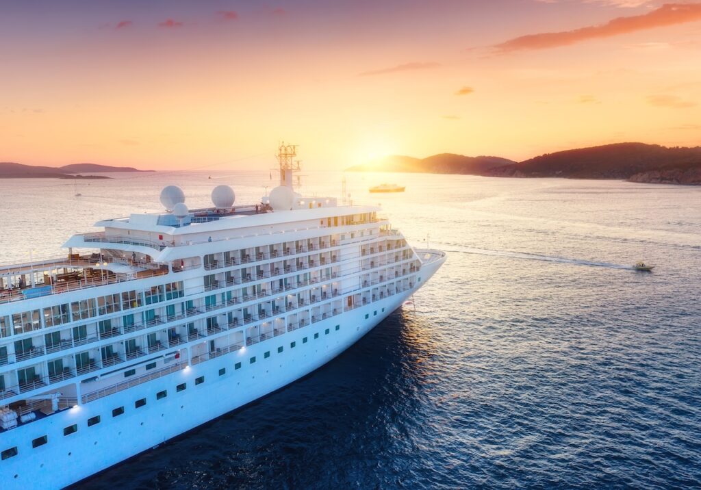A large, beautiful cruise ship anchored at sunset near an island, symbolizing the luxury transport for an escape to Saint Barthélemy on a cruise itinerary.