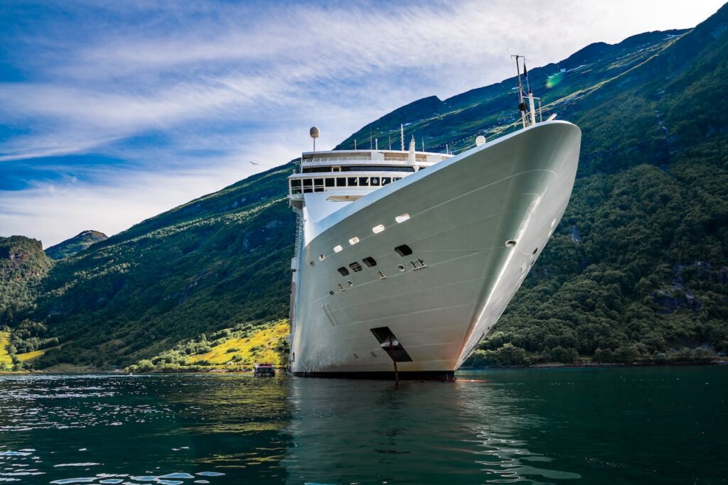 The bow of a luxury cruise ship navigating a steep, mountainous fjord, symbolizing an elegant expedition voyage to remote scenic regions.