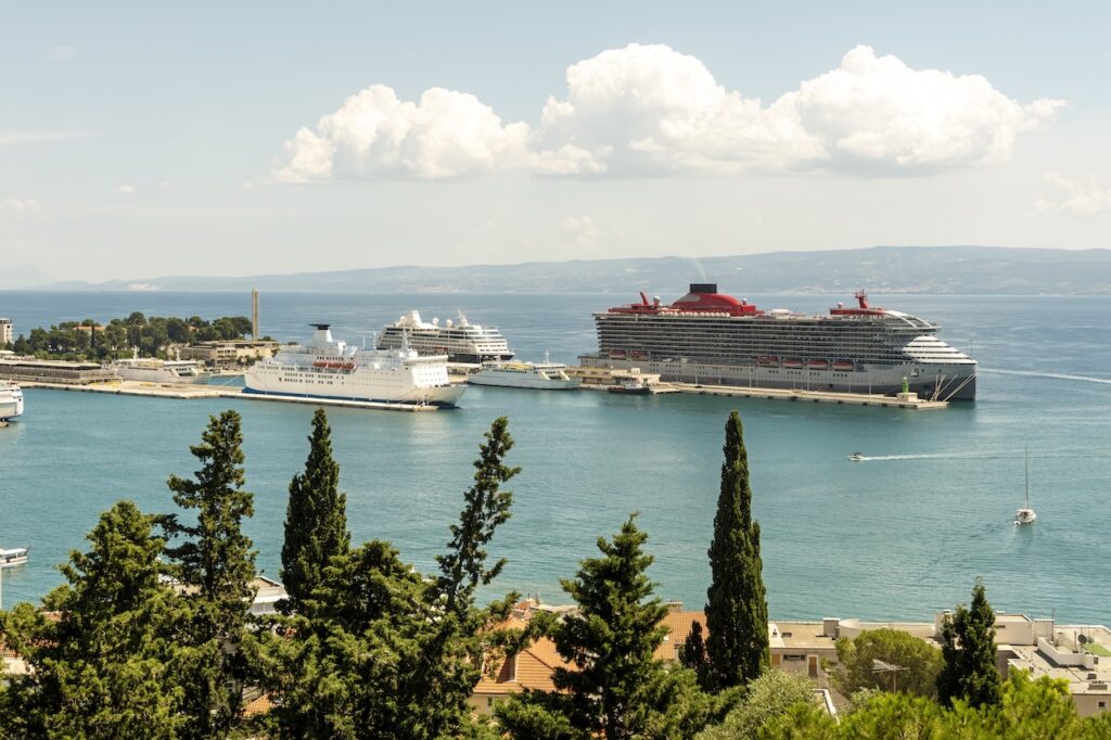 Elevated view of a harbor with a large cruise ship and a smaller white vessel docked alongside a bustling European city.