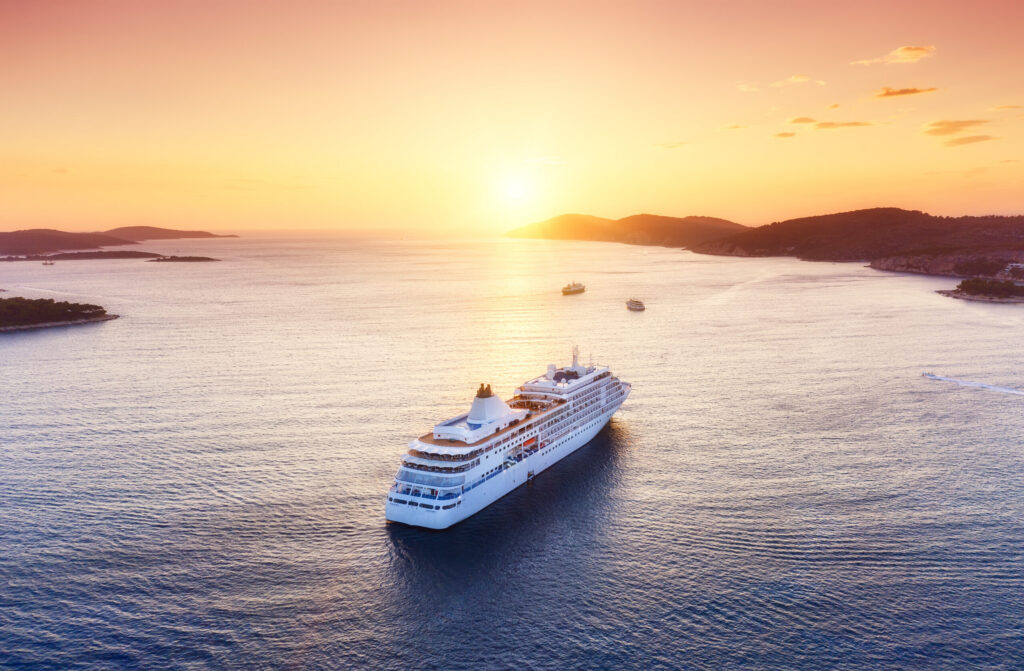 Aerial view of a majestic white ship sailing through calm coastal waters at sunset, a perfect illustration of luxury cruising.