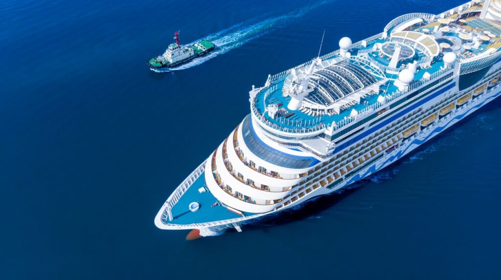 Aerial view of a large modern cruise ship sailing on the open ocean with a tugboat, highlighting luxury travel, cruising, and maritime transport.