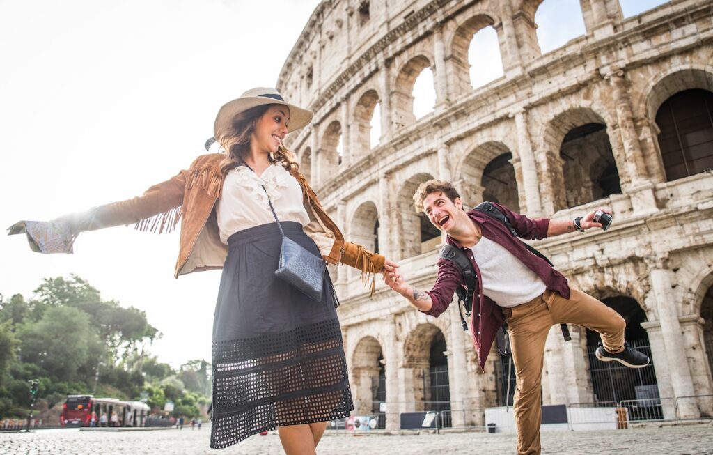 Joyful couple taking a photo in front of the ancient Colosseum in Rome, highlighting a happy and romantic cultural travel experience.