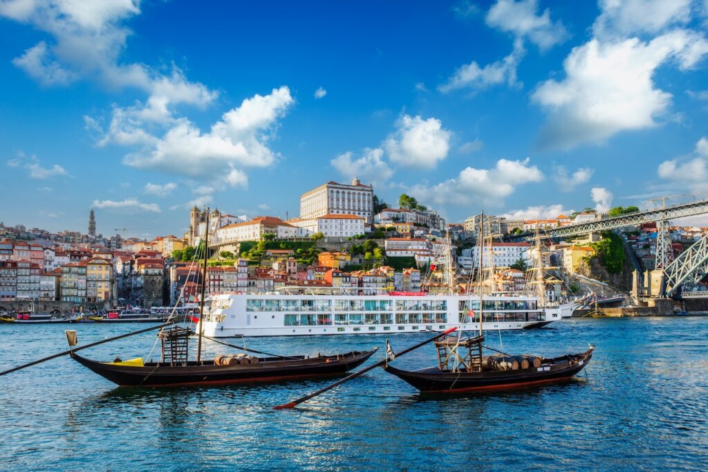 Traditional boats on the Douro River in Porto, Portugal, with terraced vineyards and historic riverside buildings in the background