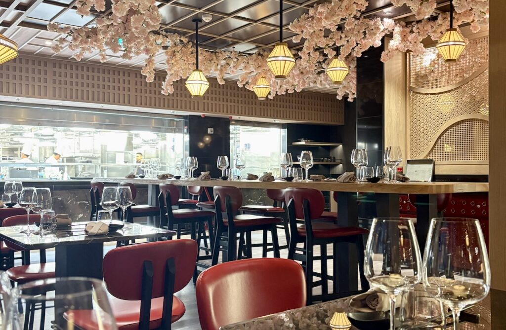Elegant and modern Asian-inspired restaurant interior with red seating, a chef's counter view, and decorative cherry blossoms, highlighting high-end dining and culinary travel.