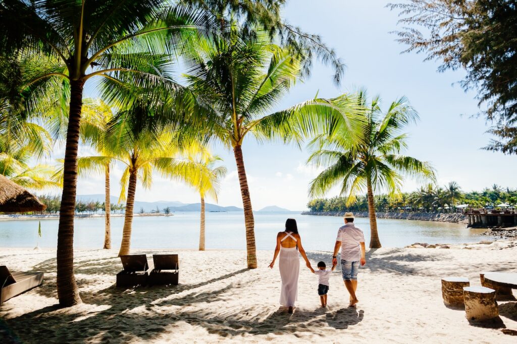 Family walking on a sunny tropical beach under palm trees, capturing a beautiful moment for a memorable family vacation getaway.