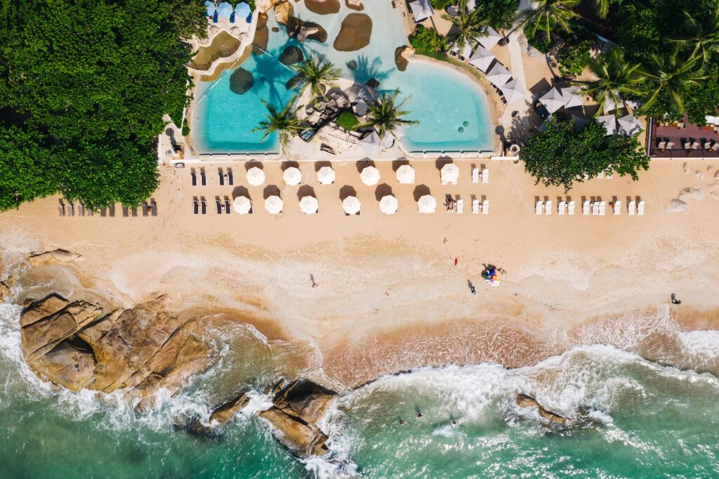 Top-down view of a stunning tropical beach and turquoise ocean with a luxury resort and swimming pool, ideal for planning an exotic beach vacation getaway.