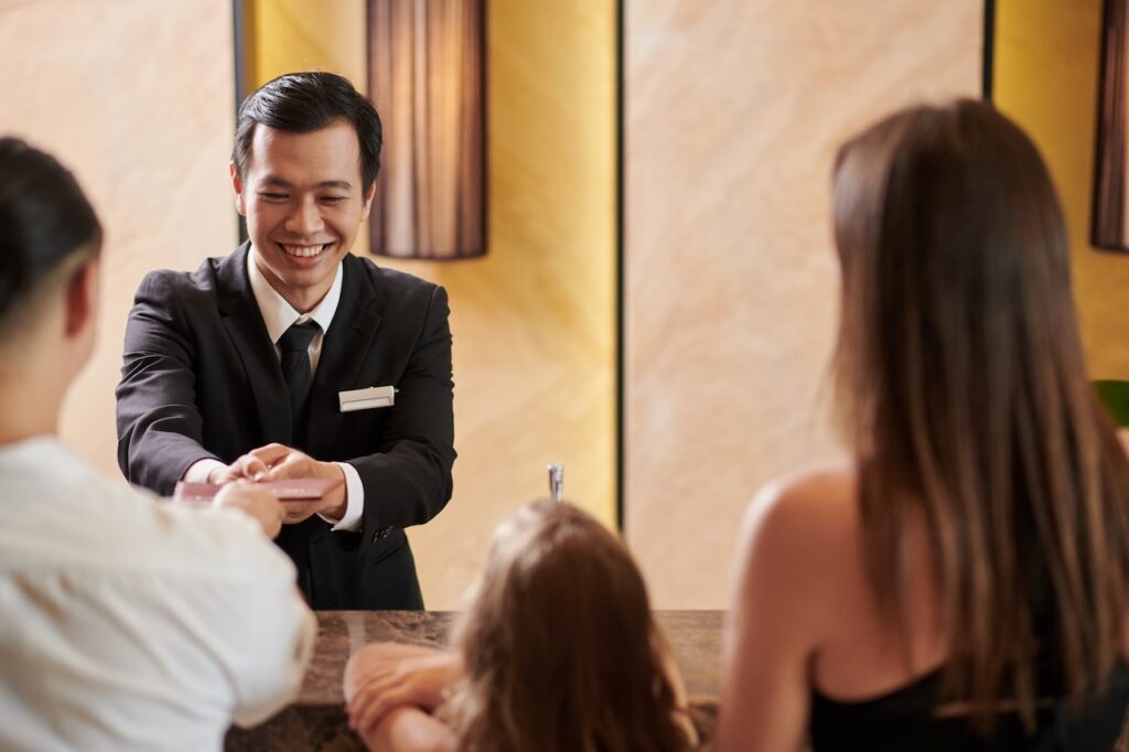 Hotel concierge smiling and handing a key card to a family at the front desk, representing luxury service when booking Hyatt Privé with points.