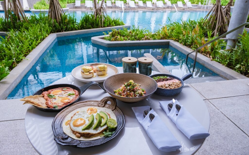 An elaborate breakfast spread served poolside in a lush, tropical Thai resort, illustrating the daily complimentary breakfast perk.