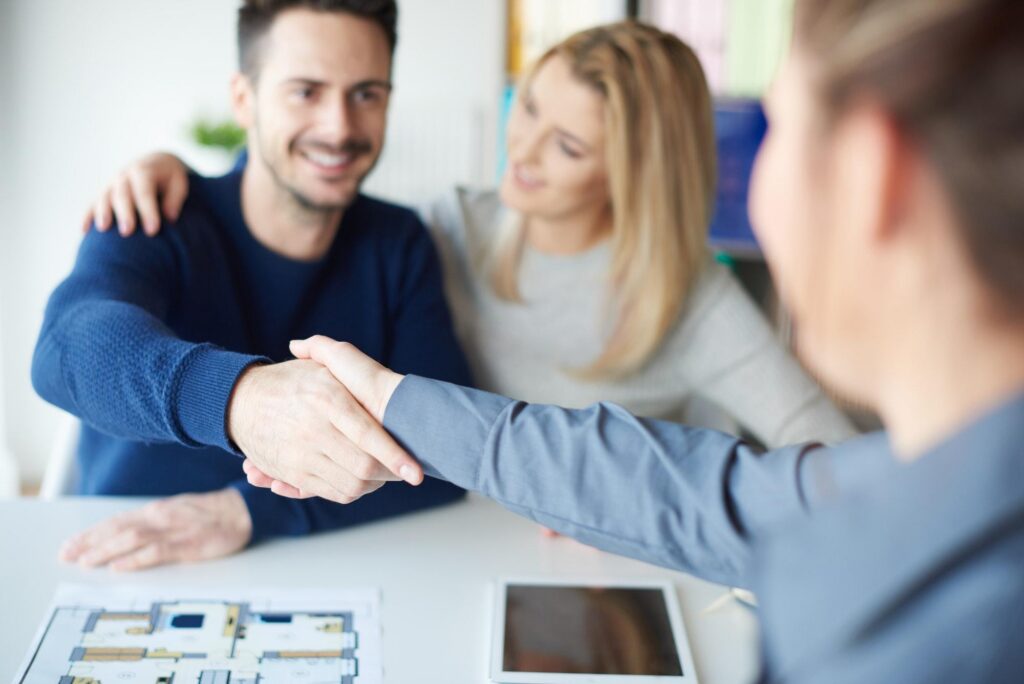 Two colleagues shake hands in an office while a third observes, symbolizing successful collaboration with a luxury travel agency,.