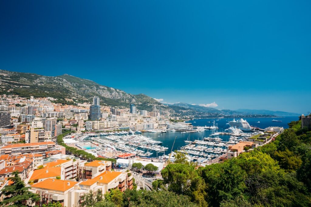 Aerial view of a vibrant Mediterranean city and harbor, showcasing luxury yachts docked in the marina and high-end coastal travel destinations.
