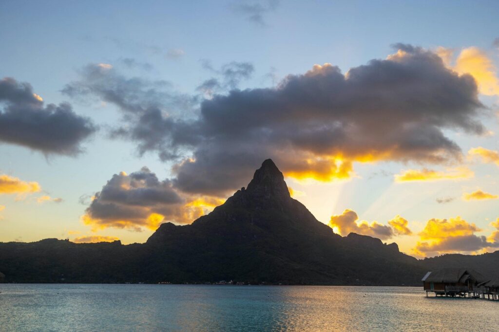 The iconic silhouette of Mount Otemanu at sunset, reflecting the tropical beauty of Bora Bora with luxury overwater bungalows in the distance.