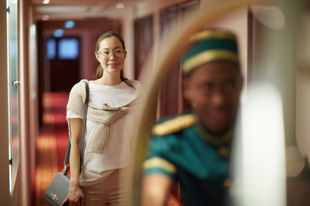 A woman smiling while walking through a brightly lit, modern stateroom hallway on a cruise ship. This image captures the excitement of exploring a new cabin category, a common experience for travelers who successfully use the MSC upgrade bidding program to move from a standard room to a premium suite or the luxury Yacht Club.