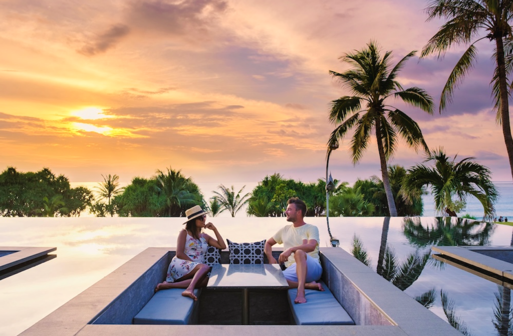 Romantic couple sitting in a resort infinity pool at sunset, highlighting the luxurious and exclusive atmosphere for an adults-only beach escape.