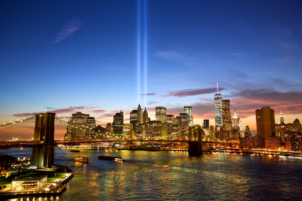 The New York City skyline illuminated at dusk with the twin towers and the Tribute in Light beams, commemorating September 11th, reflecting resilience and remembrance.