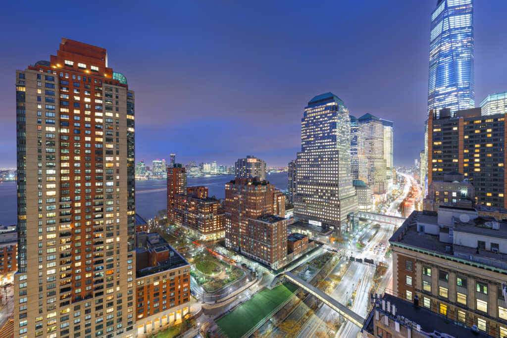 Lower Manhattan skyline at dusk with One World Trade Center and luxury New York City hotels nearby.