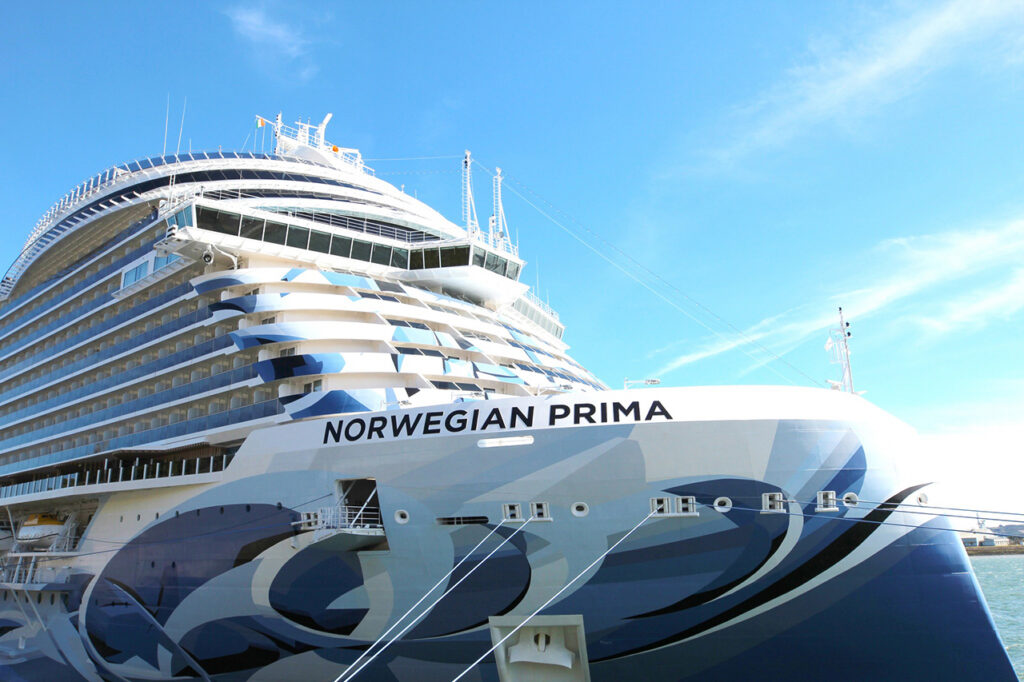 A high-angle view of the exclusive Norwegian Haven sundeck on the Norwegian Prima, featuring a modern infinity-edge pool that overlooks the ocean. Guests relax on luxury loungers near a glass-walled outdoor sauna, capturing the "ship-within-a-ship" sanctuary designed by Piero Lissoni.