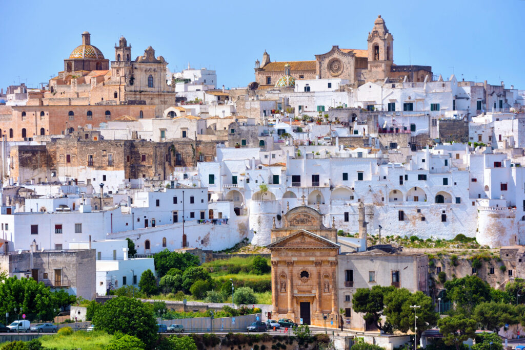 A panoramic view of the "White City" of Ostuni featuring whitewashed buildings, sun-drenched stone cathedrals, and classic Italian architecture, a top destination when you travel Puglia.