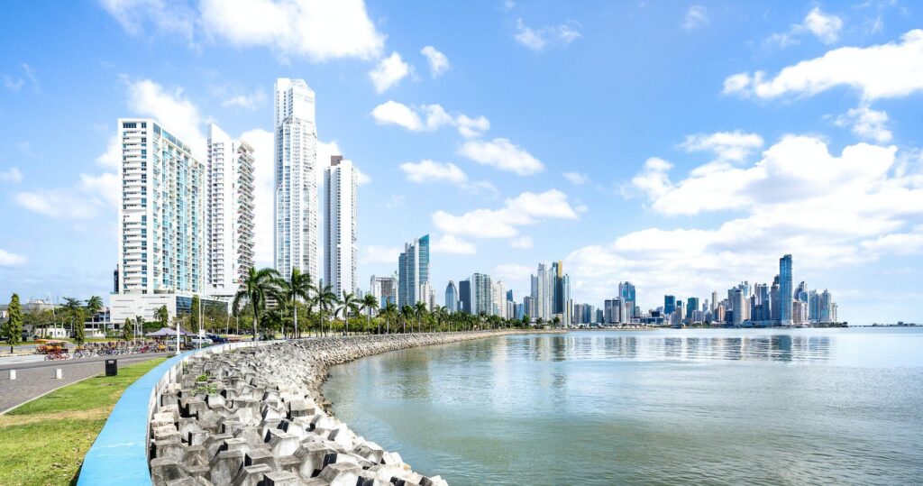 A wide view of the modern skyline along Panama City Beach, featuring high-rise buildings and a palm-lined waterfront under a bright sky.