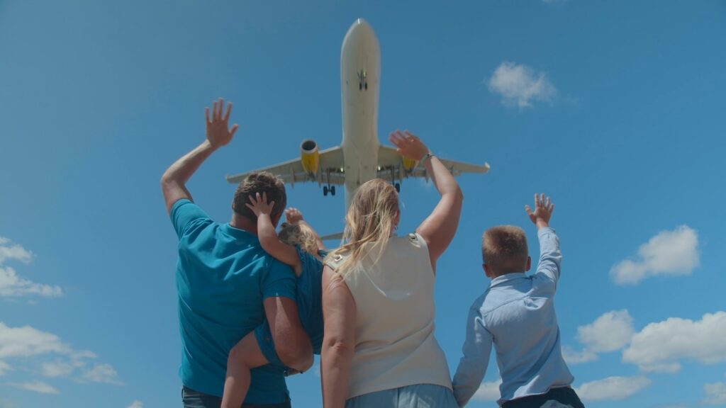Family with two children waving goodbye as a commercial airplane lands overhead, symbolizing the start or end of a memorable family travel vacation.