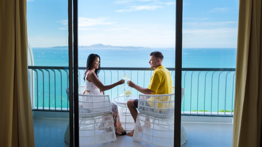 Romantic couple toasting on a private balcony with a stunning turquoise ocean view, highlighting a luxury resort getaway vacation.