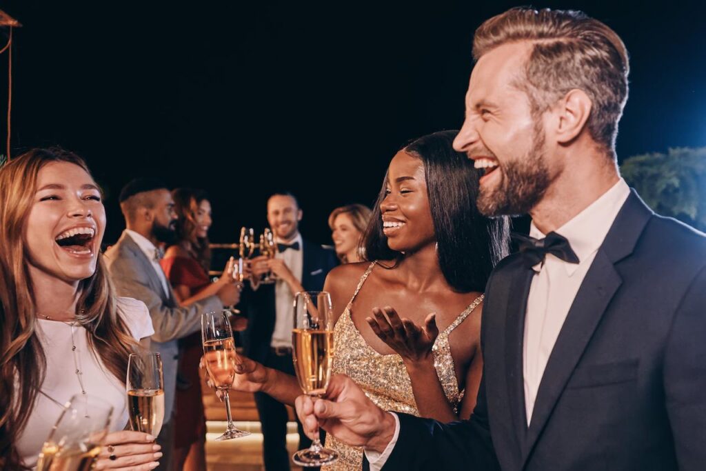 Friends in formal attire toast with champagne at an elegant evening event, dressed beyond standard resort casual clothing.