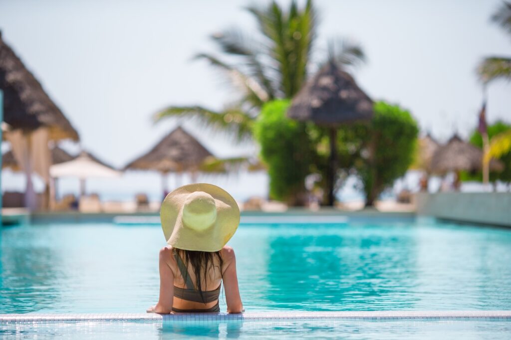 Woman relaxing in a luxury resort swimming pool with a sun hat, highlighting a serene and tropical getaway vacation.