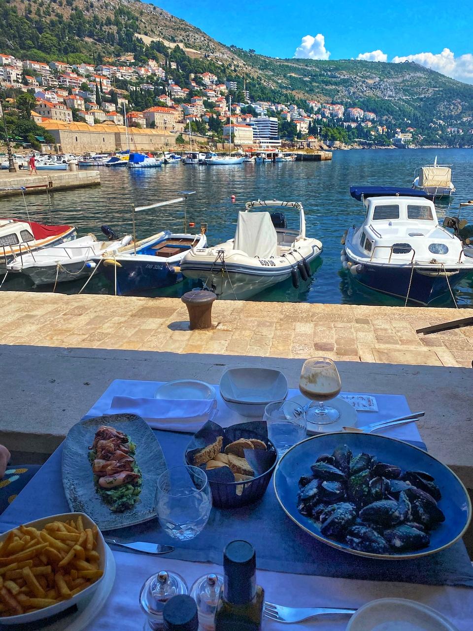 Small boats moored at a harbor with stone docks, offering a view of the terracotta-roofed buildings and lush hills of old town Dubrovnik.
