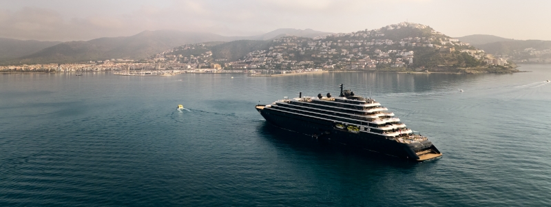 A sleek, modern superyacht from the Ritz-Carlton Yacht Collection anchored in a turquoise bay.