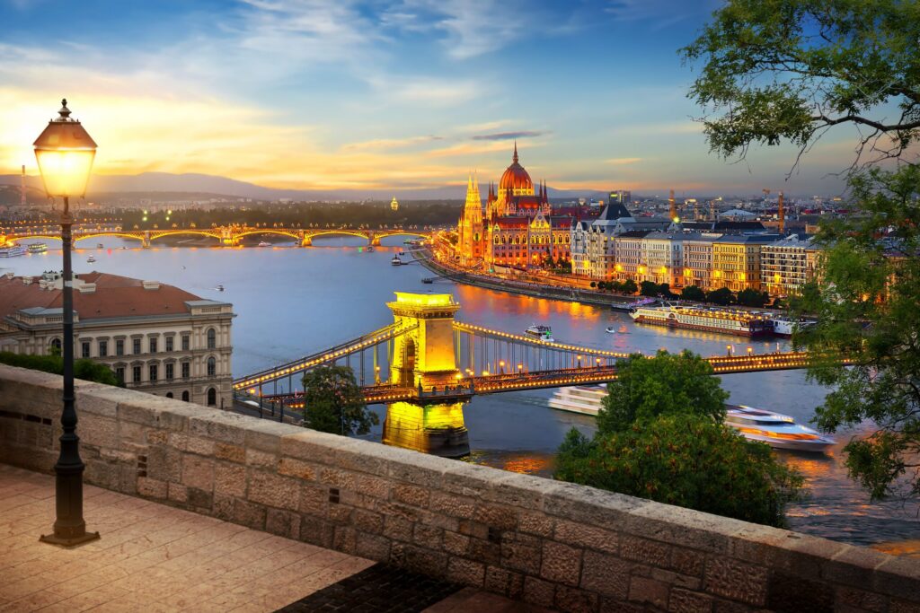 A dramatic twilight view of the illuminated Chain Bridge and the Hungarian Parliament Building in Budapest, spanning the Danube River, symbolizing a historical European river cruise.
