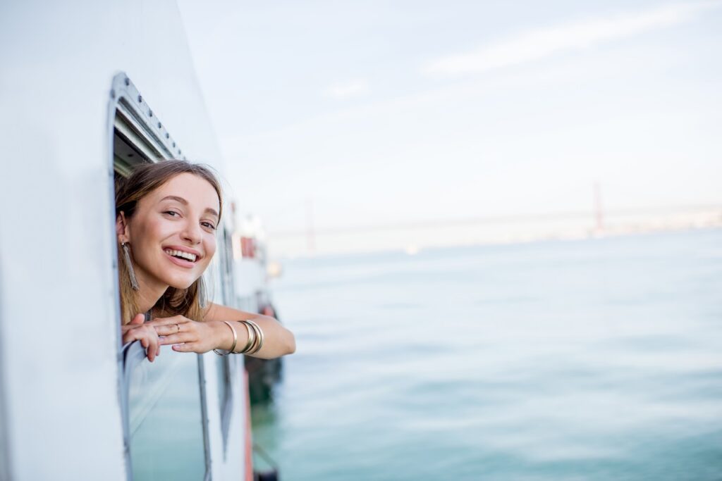 Smiling woman leaning out from a river cruise ship while sailing in Europe, enjoying the scenic water views.